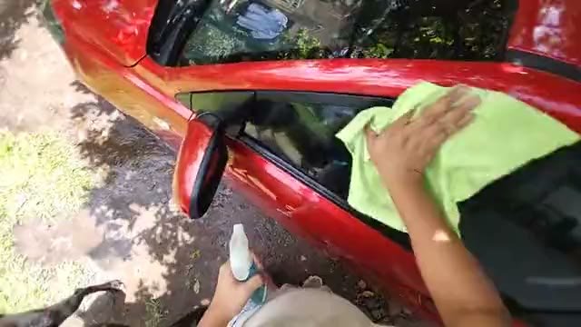 Mão passando um pano na lataria e no vidro de um carro vermelho, gravado em primeira pessoa